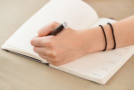 La imagen es un primer plano de la mano de una persona escribiendo.