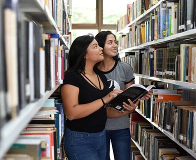 Dos estudiantes consultando un libro junto a uno de los estantes de una biblioteca universitaria. (Foto: Archivo ODI)
