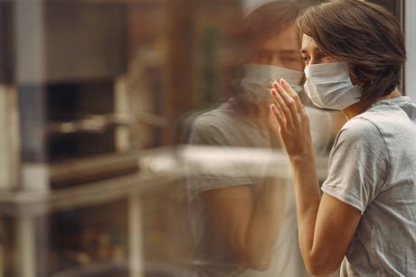 Mujer con mascarilla viendo a través de una ventana.