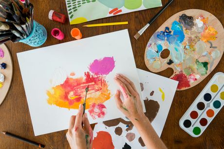 Imagen en la que se aprecian las manos de una persona con varios materiales de arte: lienzo, pinturas, paleta para mezclar pintura.