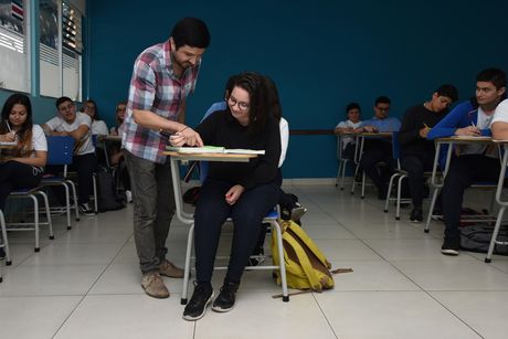 Profesor aclarando dudas a una estudiante que está sentada en su clase.
